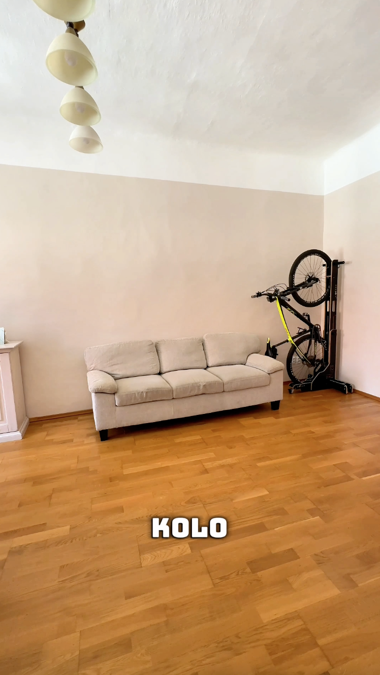 Světlý obývací pokoj s béžovou pohovkou, dřevěnou podlahou a stojícím kolem ve stojanu BIKERECT u zdi.
