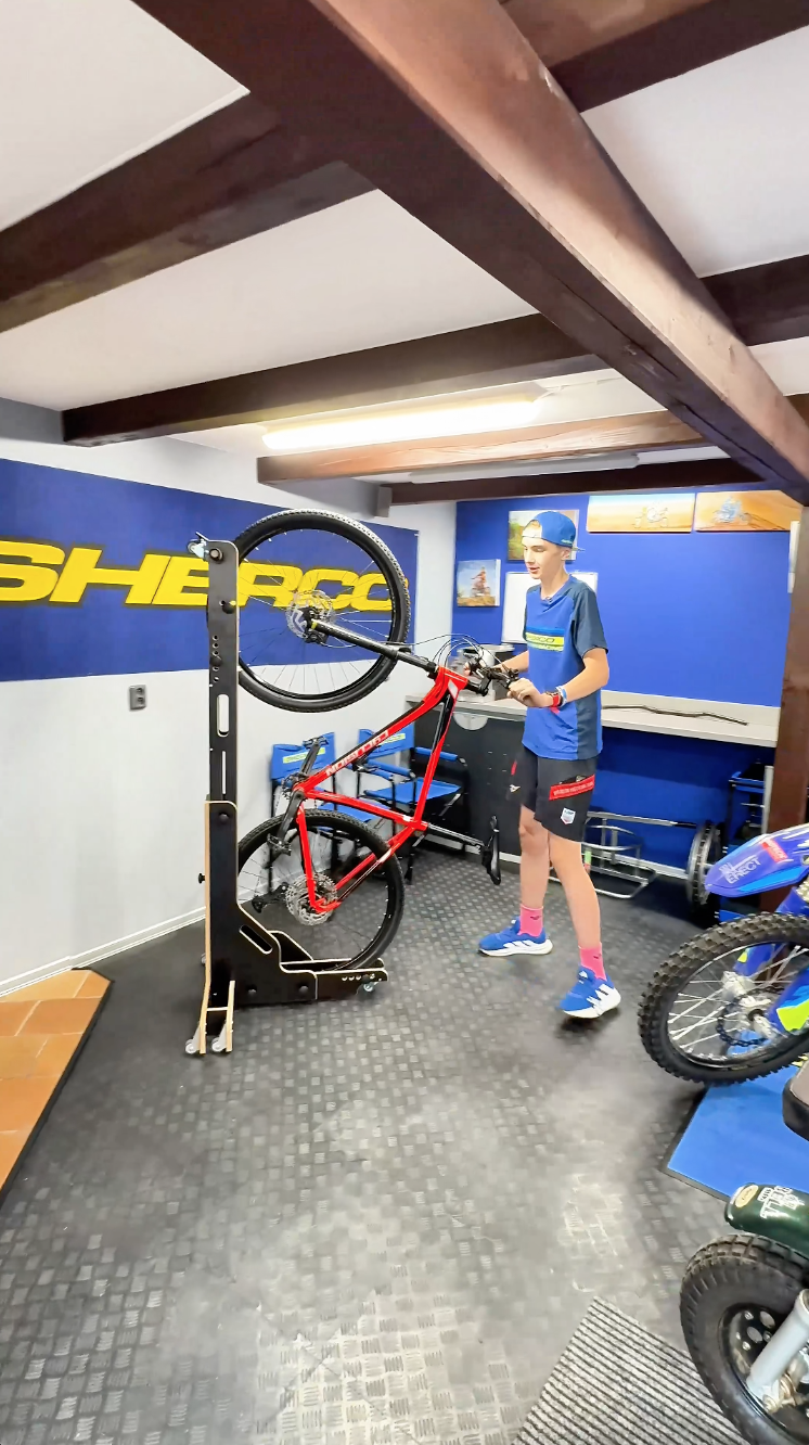 Muž v dílně drží kolo ve stojanu BIKERECT, modré stěny.